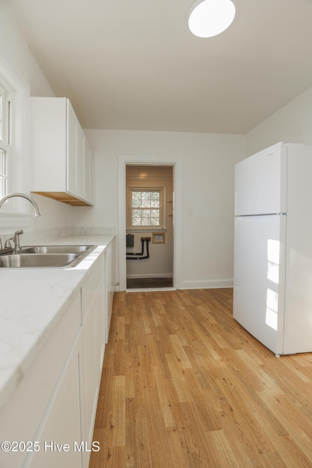 kitchen with light countertops, light wood-style flooring, freestanding refrigerator, white cabinets, and a sink