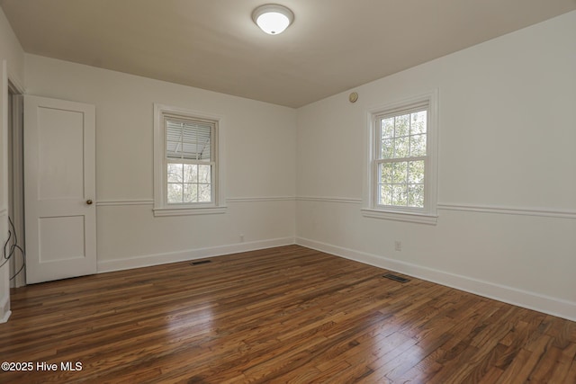 unfurnished room featuring baseboards, visible vents, and dark wood finished floors