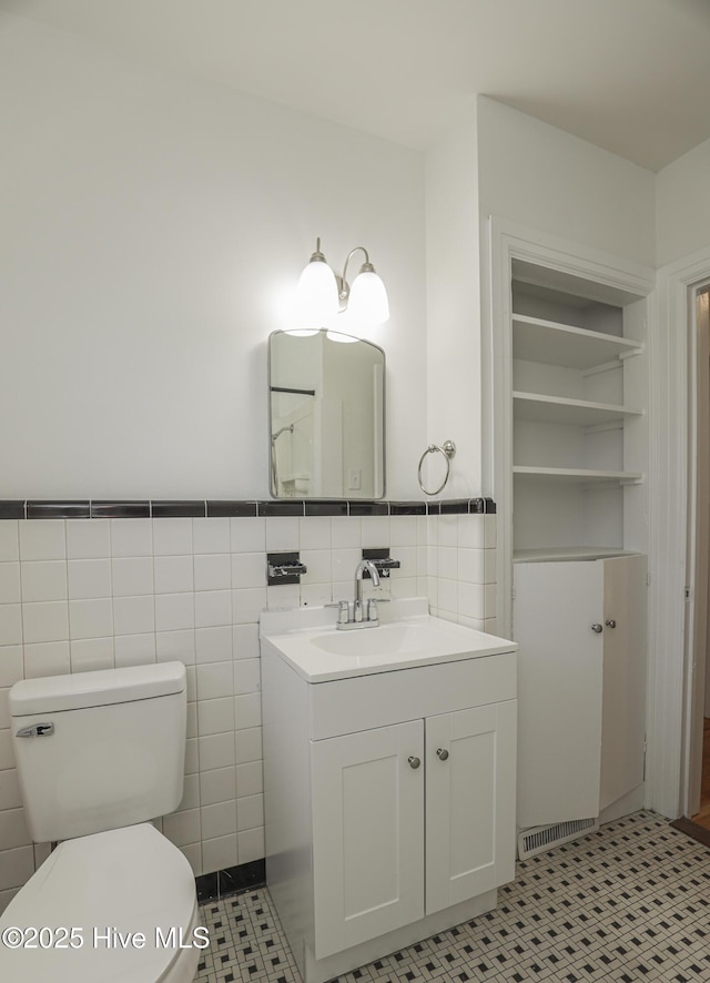 bathroom featuring built in features, tile walls, toilet, wainscoting, and vanity