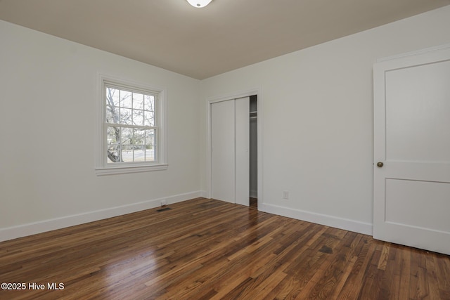 unfurnished bedroom featuring dark wood-style floors, visible vents, baseboards, and a closet