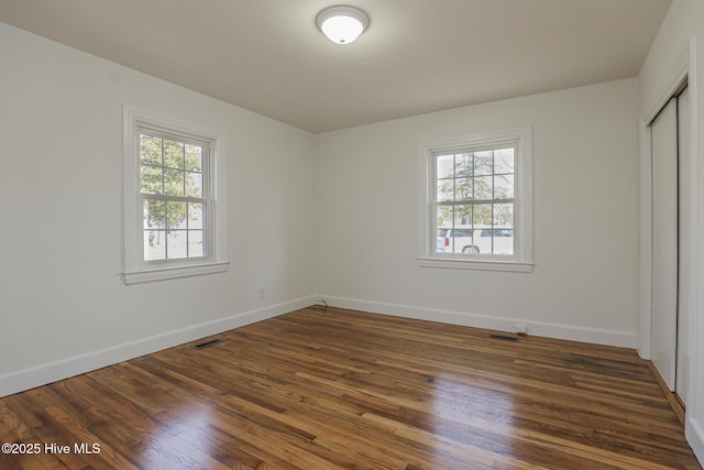 unfurnished bedroom featuring visible vents, dark wood finished floors, and multiple windows