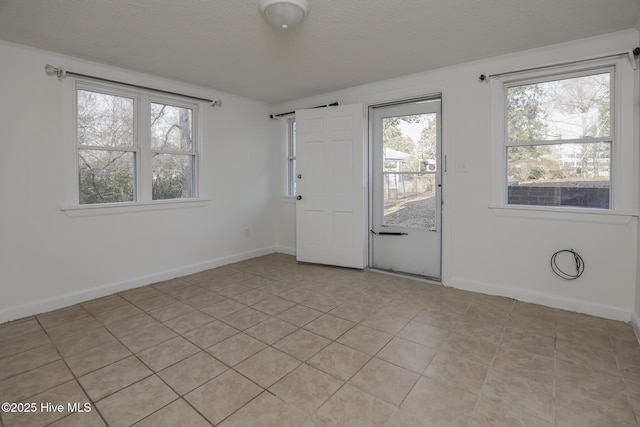 empty room with a textured ceiling, light tile patterned flooring, and baseboards