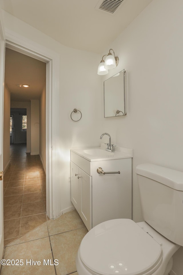 half bathroom with visible vents, toilet, vanity, baseboards, and tile patterned floors