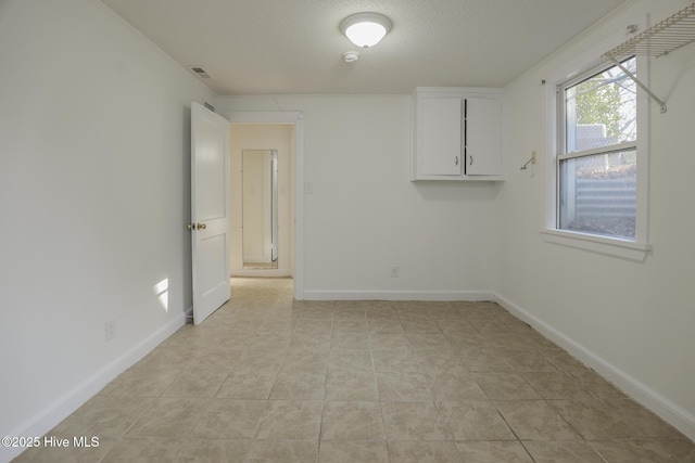 empty room featuring a textured ceiling, baseboards, and light tile patterned floors