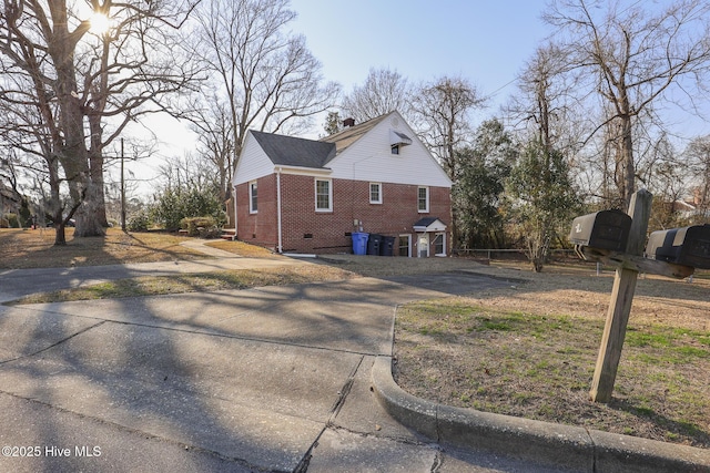 view of side of property featuring concrete driveway, brick siding, a chimney, and crawl space