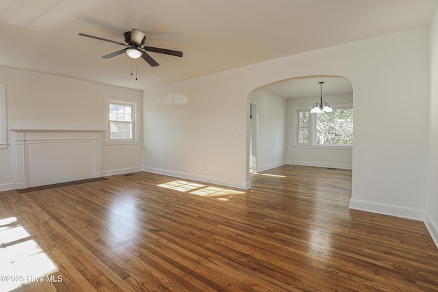 unfurnished room featuring baseboards, arched walkways, wood finished floors, and ceiling fan with notable chandelier