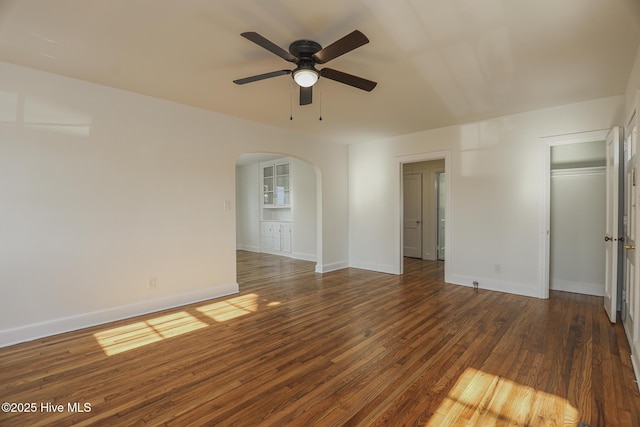 spare room featuring arched walkways, ceiling fan, wood finished floors, and baseboards