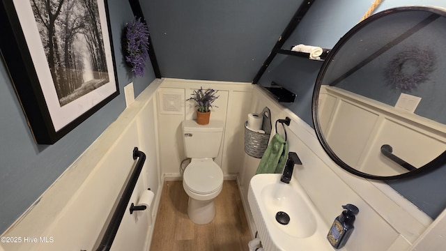 half bath with wainscoting, wood finished floors, toilet, and a decorative wall