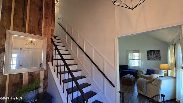 stairs featuring high vaulted ceiling, a chandelier, wood finished floors, and a decorative wall