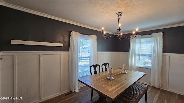 dining area with a wainscoted wall, a textured ceiling, an inviting chandelier, and wood finished floors