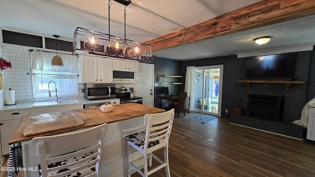 kitchen featuring stainless steel appliances, dark wood-type flooring, a sink, white cabinets, and beamed ceiling