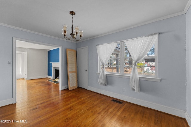 unfurnished dining area with a fireplace, visible vents, a chandelier, and crown molding