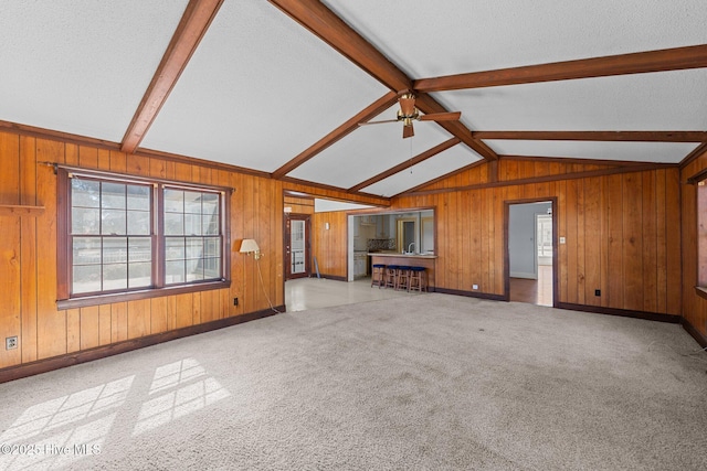 unfurnished living room featuring vaulted ceiling with beams, a ceiling fan, carpet flooring, wood walls, and a textured ceiling