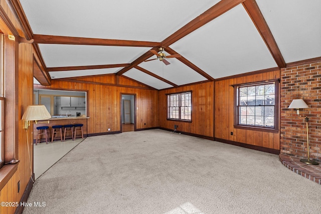 unfurnished living room featuring carpet floors, vaulted ceiling with beams, wood walls, and ceiling fan