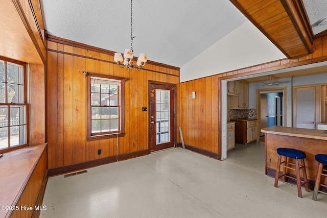 dining room with finished concrete flooring, wooden walls, visible vents, vaulted ceiling, and a chandelier