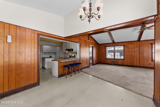 kitchen featuring vaulted ceiling with beams, open floor plan, wooden walls, concrete flooring, and ceiling fan with notable chandelier