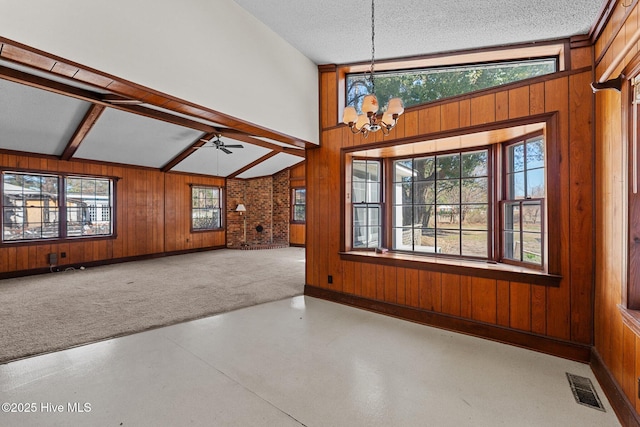 unfurnished living room with a textured ceiling, wood walls, ceiling fan with notable chandelier, and visible vents