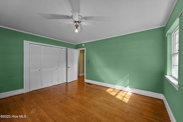 unfurnished bedroom featuring baseboards, a closet, wood finished floors, and crown molding