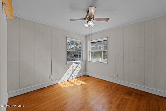 empty room with ceiling fan, wood finished floors, visible vents, and baseboards