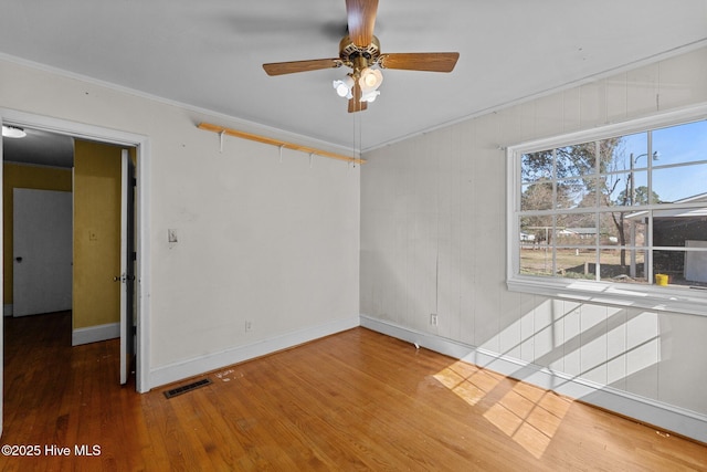 spare room with baseboards, visible vents, a ceiling fan, wood finished floors, and crown molding