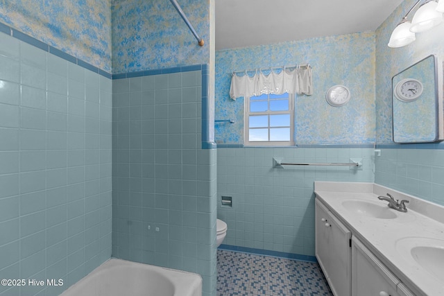 bathroom with a wainscoted wall, double vanity, toilet, a sink, and wallpapered walls