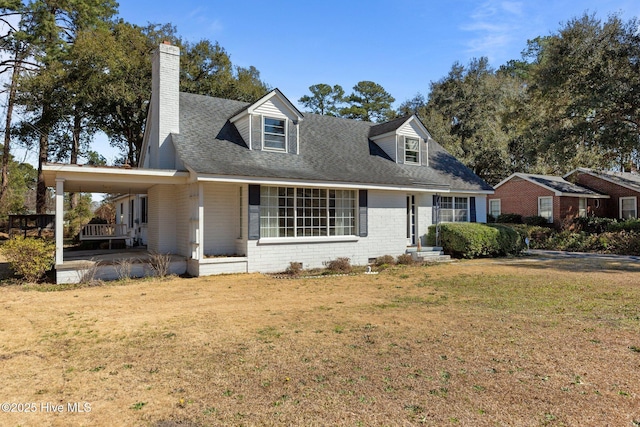 view of front of property with a shingled roof, a chimney, a front lawn, and brick siding