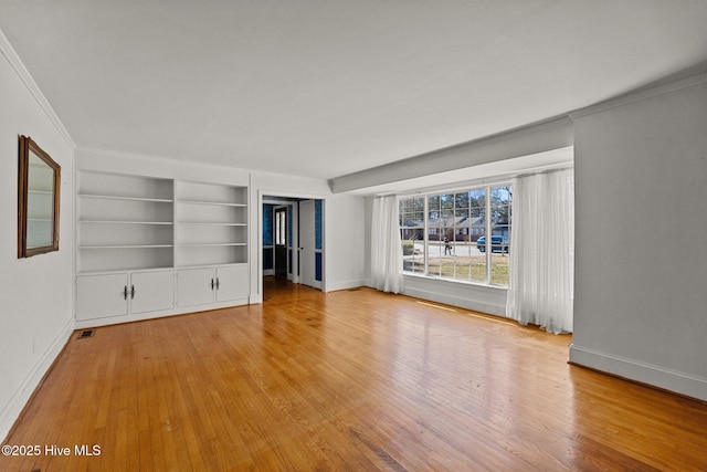 unfurnished living room with visible vents, built in shelves, baseboards, and wood finished floors