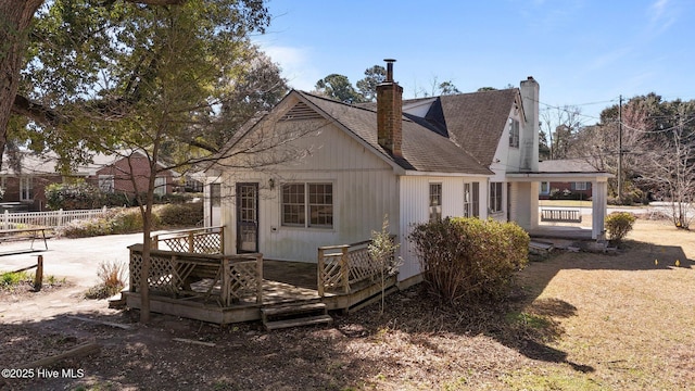 view of front of home with a shingled roof, a chimney, fence, and a deck