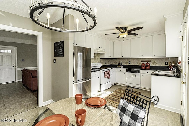 kitchen featuring dark countertops, white appliances, white cabinets, and a sink