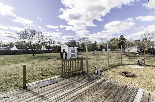 deck featuring a fire pit, a lawn, a fenced backyard, an outbuilding, and a storage unit