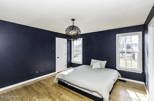 unfurnished bedroom with multiple windows, a notable chandelier, baseboards, and wood finished floors