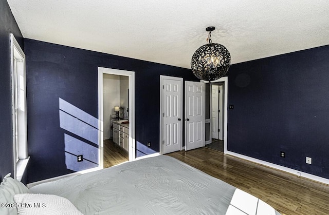 bedroom featuring baseboards, wood finished floors, ensuite bathroom, an inviting chandelier, and a textured ceiling