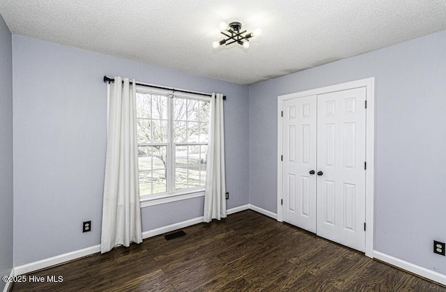 unfurnished bedroom featuring dark wood-style floors, visible vents, multiple windows, and baseboards