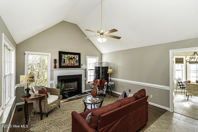 tiled living area with a ceiling fan, a fireplace with raised hearth, high vaulted ceiling, and baseboards