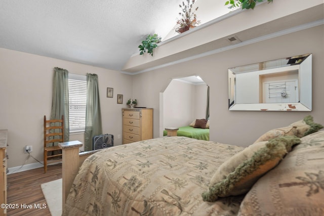 bedroom featuring baseboards, vaulted ceiling, wood finished floors, arched walkways, and a textured ceiling