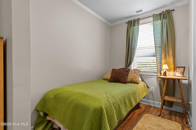 bedroom featuring wood finished floors, baseboards, visible vents, a textured ceiling, and crown molding