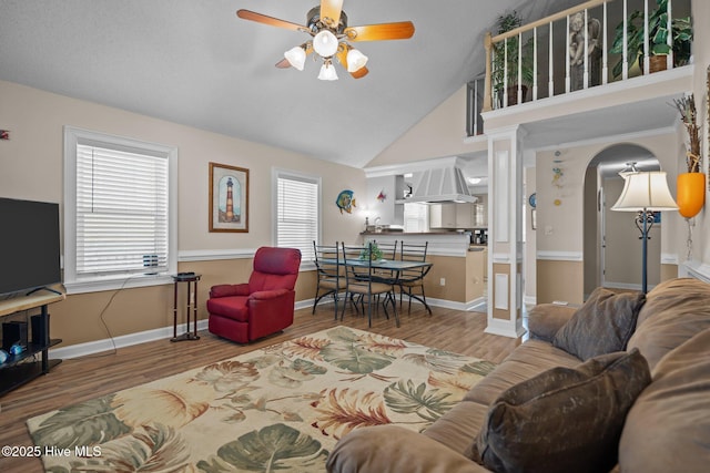 living area with baseboards, wood finished floors, arched walkways, high vaulted ceiling, and a ceiling fan