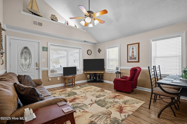 living area featuring visible vents, lofted ceiling, wood finished floors, and a ceiling fan