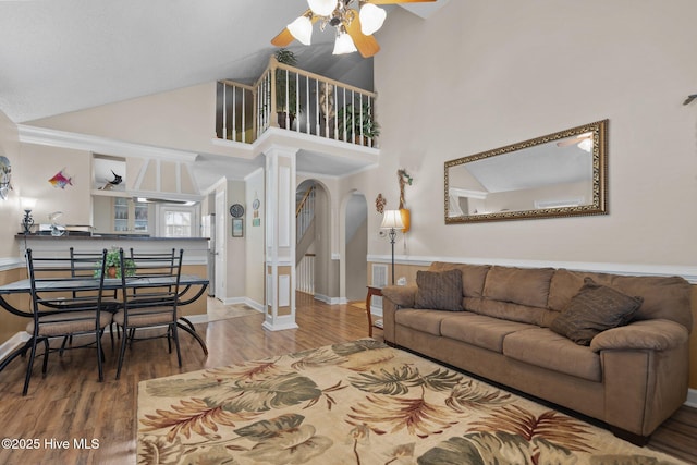 living room featuring ceiling fan, wood finished floors, arched walkways, high vaulted ceiling, and ornate columns