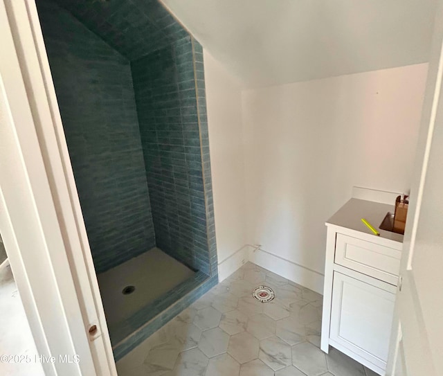 bathroom with a tile shower, tile patterned flooring, baseboards, and vaulted ceiling