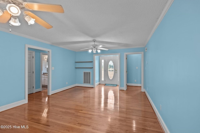 unfurnished living room featuring a textured ceiling, ornamental molding, wood finished floors, and visible vents