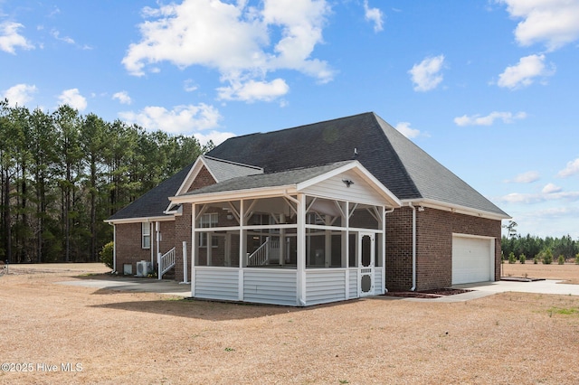 view of front of property with a shingled roof, concrete driveway, a sunroom, an attached garage, and brick siding