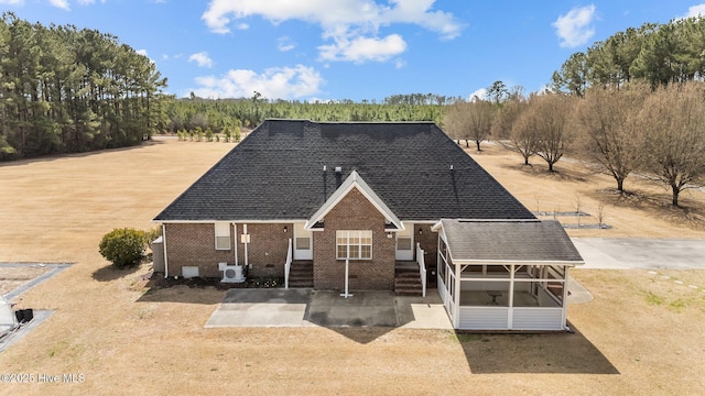 view of front of home with roof with shingles, a patio, and brick siding