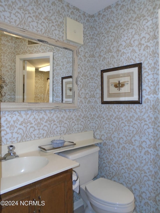 bathroom with vanity, toilet, and wallpapered walls