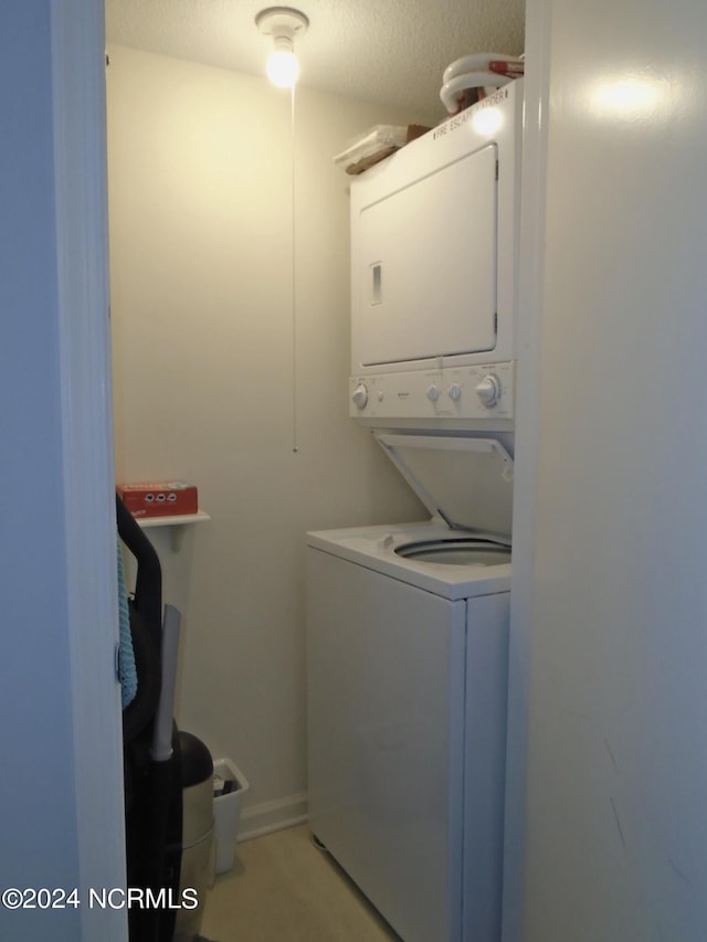 clothes washing area featuring laundry area, a textured ceiling, and stacked washer / drying machine