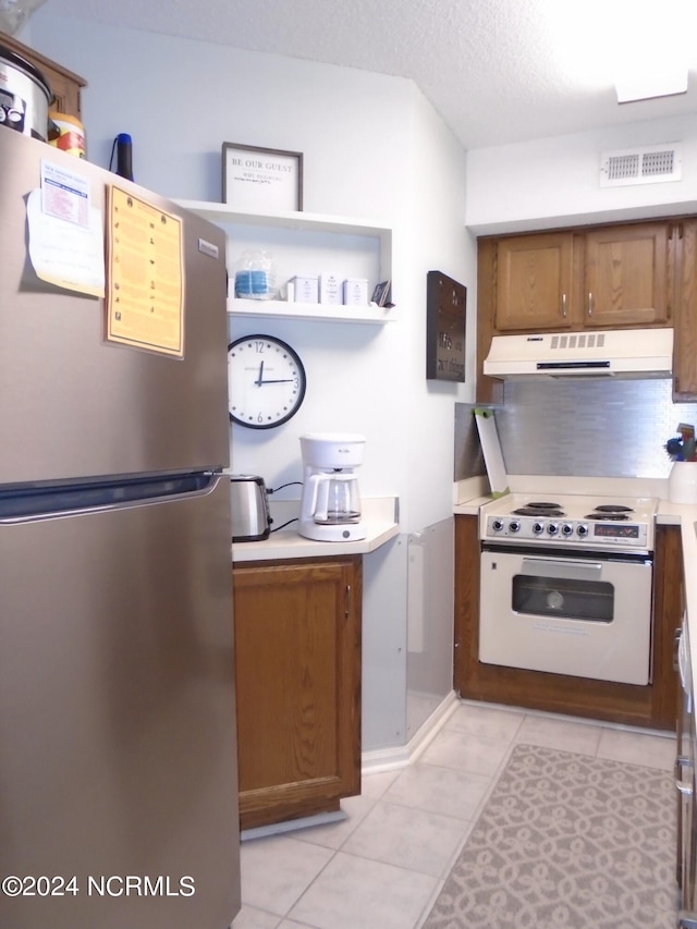 kitchen featuring light tile patterned flooring, under cabinet range hood, electric range, visible vents, and freestanding refrigerator