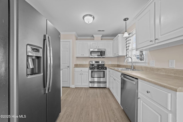 kitchen featuring appliances with stainless steel finishes, white cabinets, a sink, and ornamental molding