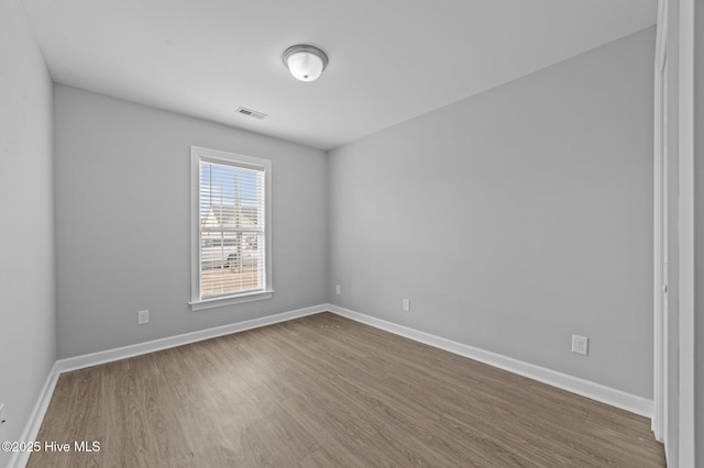 unfurnished room with dark wood-style flooring, visible vents, and baseboards