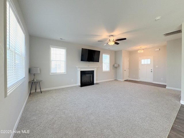 unfurnished living room with a fireplace with flush hearth, baseboards, visible vents, and ceiling fan