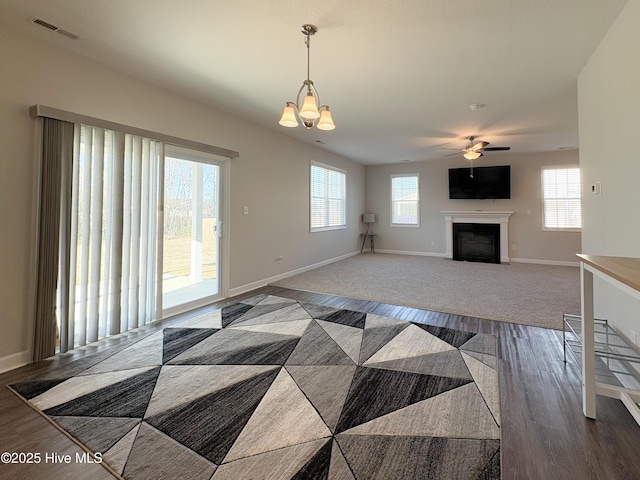 living area with visible vents, baseboards, a fireplace with flush hearth, ceiling fan with notable chandelier, and wood finished floors
